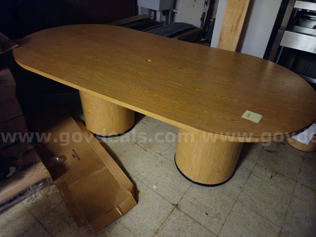 large oval conference table with a light wood-grain laminate finish and two cylindrical drum bases.