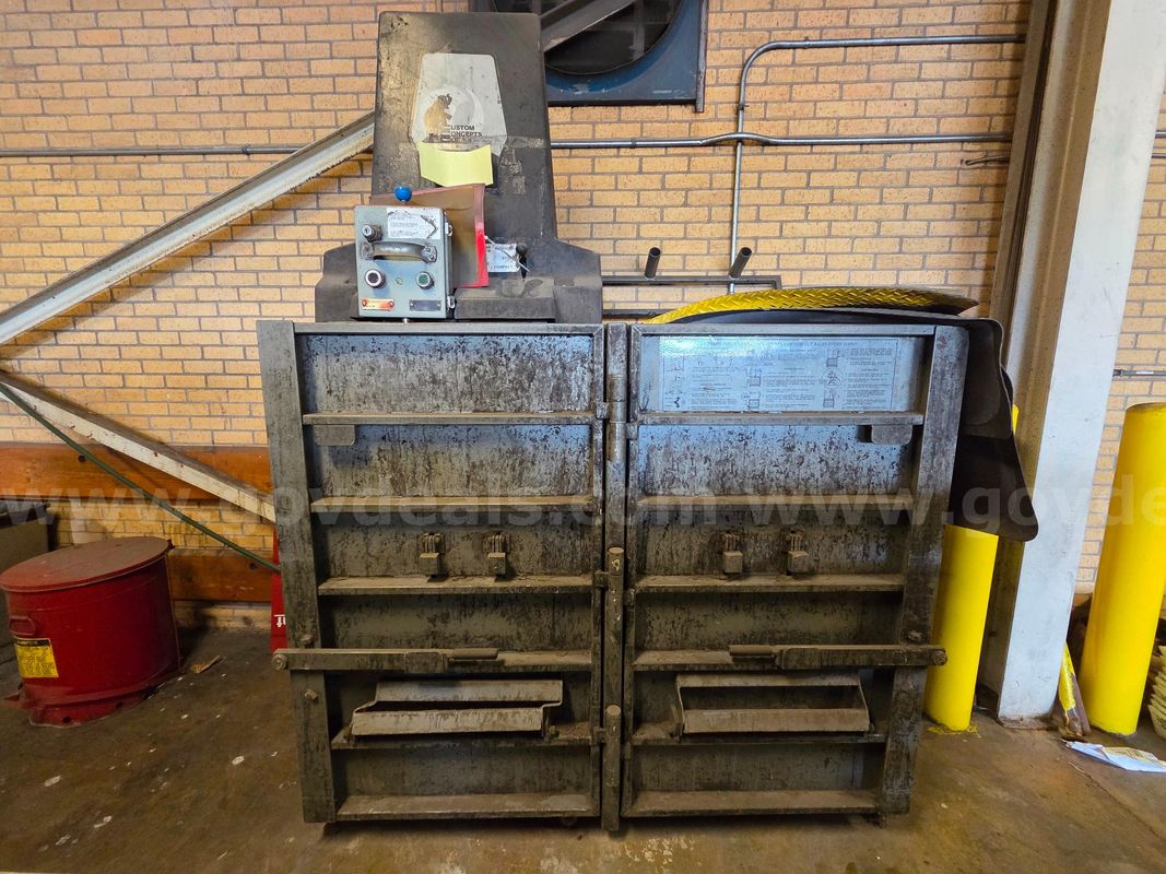 Industrial vertical trash compactor or cardboard baler used for recycling and waste management.