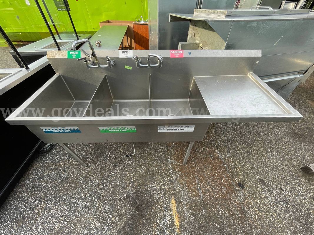 commercial stainless steel three-compartment sink with dual drainboards.